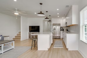 Une cuisine moderne avec des meubles blancs, un îlot central, des appareils électroménagers en acier inoxydable et un ventilateur de plafond.