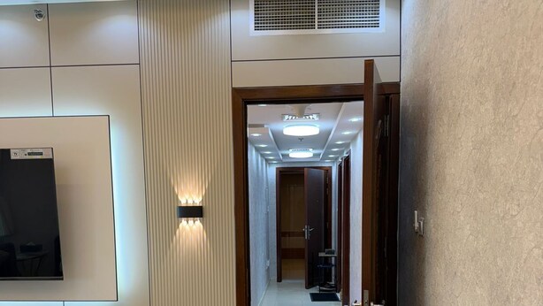 Una sala de estar moderna con un sofá gris, un televisor de pantalla plana montado en la pared y un pasillo que conduce a un dormitorio.