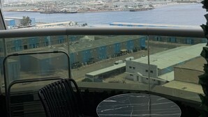 Un balcón con vistas a un paisaje urbano frente al mar, que incluye un puerto y edificios industriales.