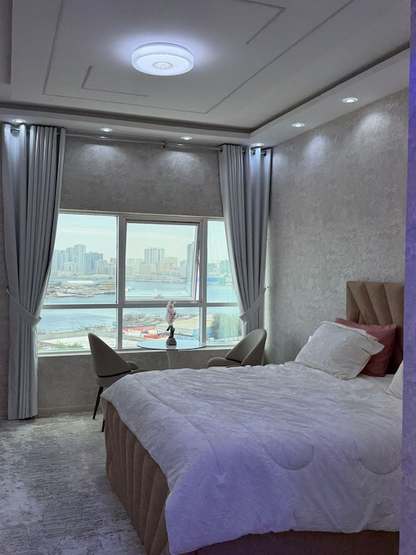 A hotel room with a large bed, a view of a cityscape through a window, and a ceiling light.