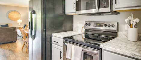 Cozinha moderna com eletrodomésticos de aço inoxidável, armários brancos e bancada de mármore.