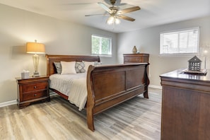 A bedroom with a wooden bed, nightstands, a dresser, a ceiling fan, and windows with blinds. - Tiger Town Retreat: Spacious Home for Groups! (Baton Rouge)