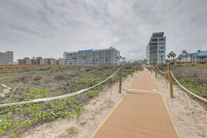 A sandy pathway leading to a building with multiple floors, surrounded by vegetation and a rope barrier. - Community Pool! Walkable South Padre Island Studio (South Padre Island)
