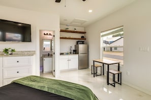 A modern kitchen with white cabinets, a microwave, and a refrigerator. There is a dining area with a table and chairs, and a TV mounted on the wall. - Community Pool! Walkable South Padre Island Studio (South Padre Island)