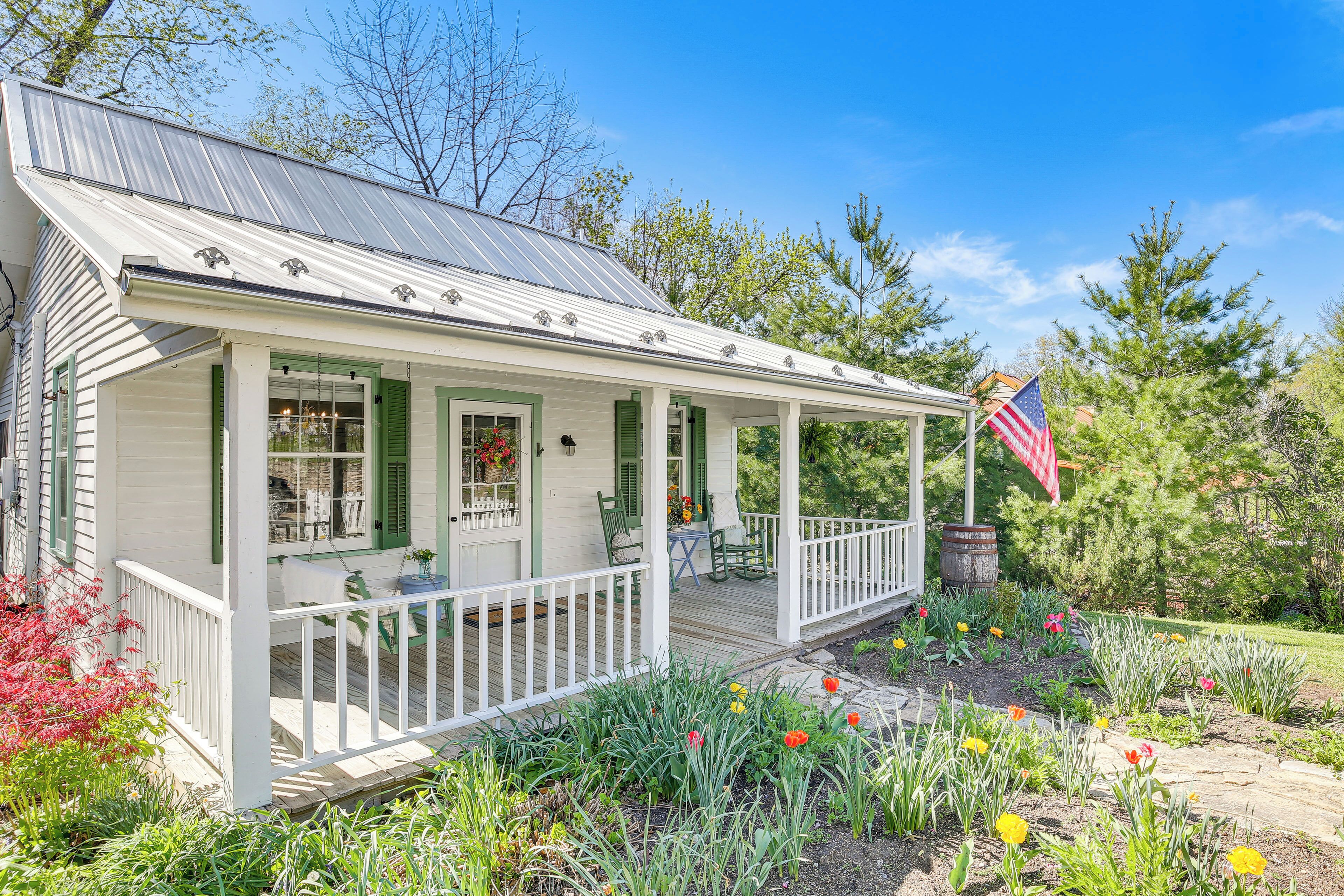A white house with a porch, green shutters, and an American flag.