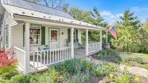 Et hvidt hus med veranda, grønne skodder og et amerikansk flag.