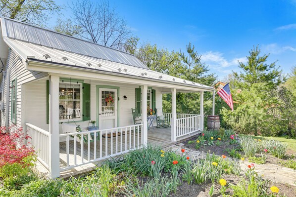 A white house with a porch, green shutters, and an American flag.