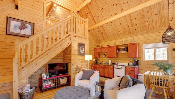Interior de una cabaña de madera con escalera, sala de estar, cocina y comedor.