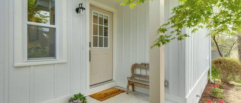 A house with a front porch, a bench, a welcome mat, and potted plants.