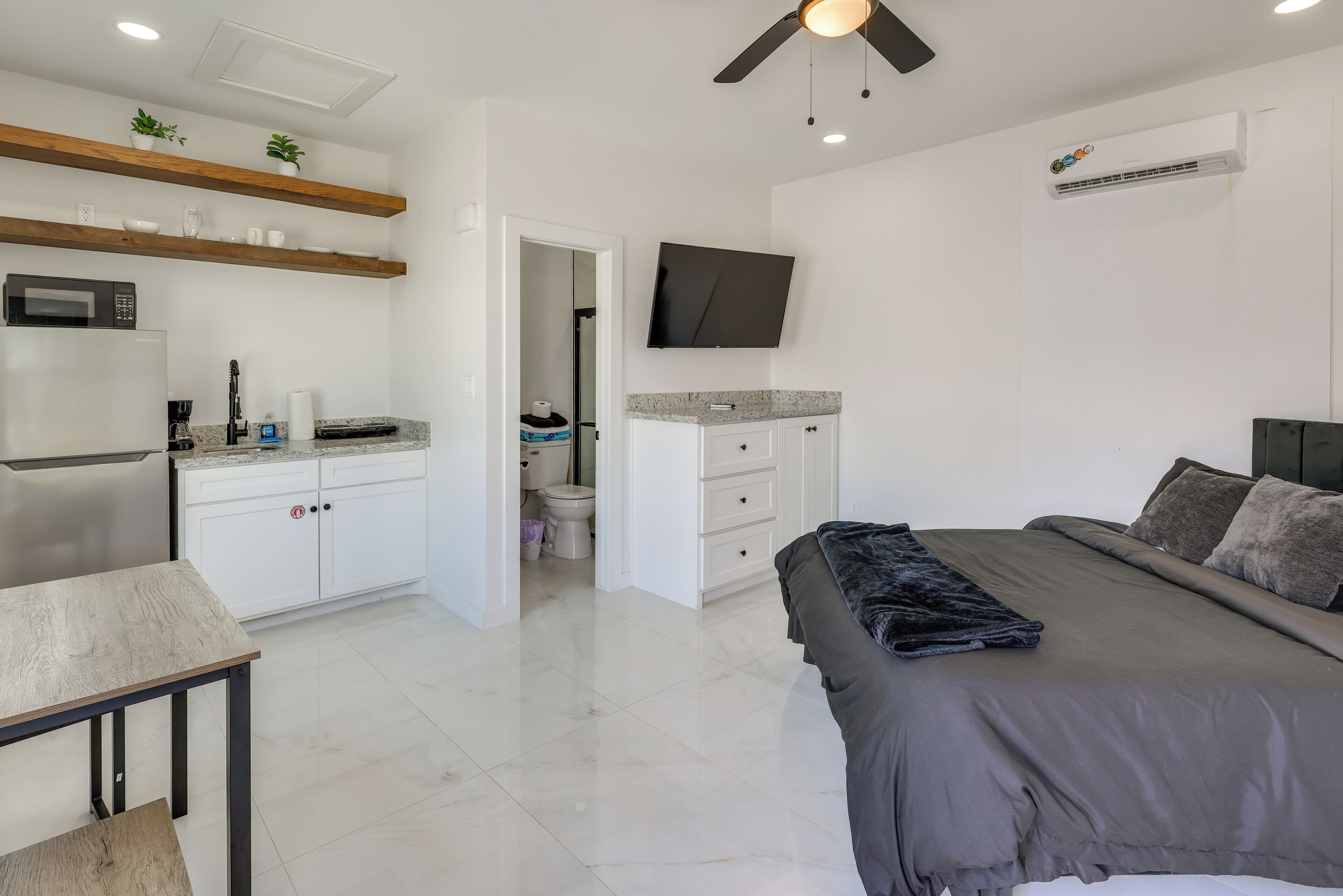 A modern bedroom with a bed, a desk, and a kitchenette.