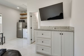 Eine moderne Küche mit weißen Schränken, einer Arbeitsplatte aus Granit, einem flachen Fernseher über den Schränken und einem Kühlschrank im Hintergrund.