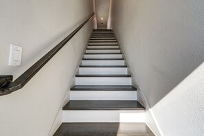 Un escalier avec des marches en bois et une rampe, menant à un palier où se trouve un interrupteur.