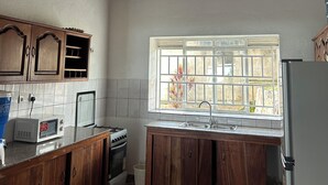 Cozinha com armários de madeira, micro-ondas, fogão e janela com vista.