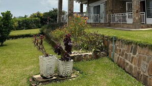 Uma casa de dois andares com alpendre, pilares de pedra e um jardim bem cuidado.