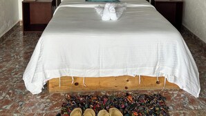 Uma cama com cabeceira de madeira, roupa de cama branca, um travesseiro verde e um par de chinelos no chão.