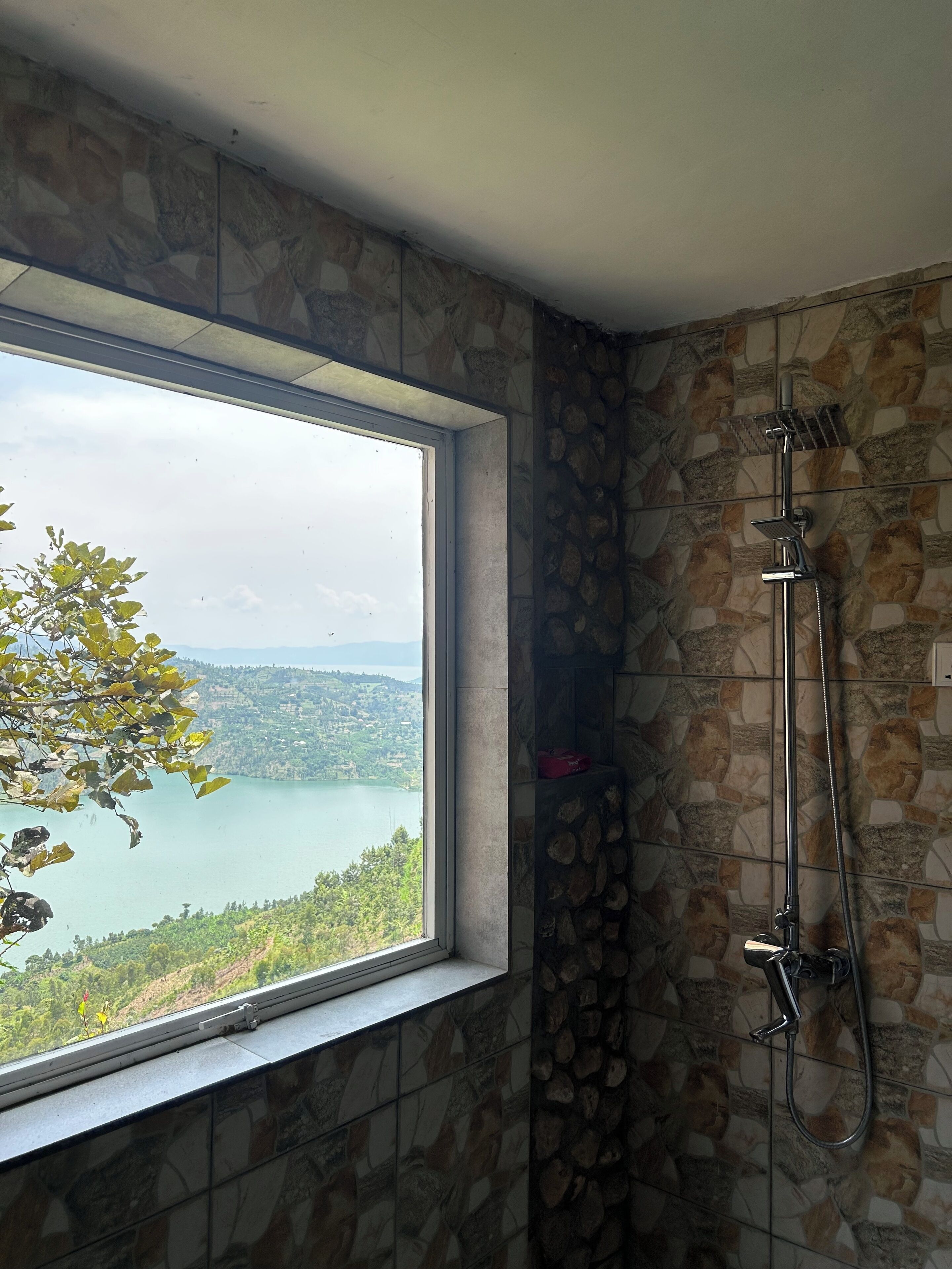 A bathroom with a shower, a window, and a stone wall.
