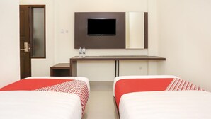 A hotel room with two beds, a TV mounted on the wall, a desk with a mirror, and a door. - Luxury Twin Stay with Free WiFi and Parking (Yogyakarta)