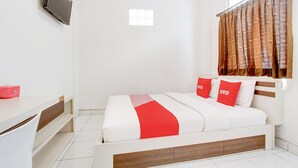Ein Hotelzimmer mit Bett, Wandfernseher, Vorhängen am Fenster und Schreibtisch mit Stuhl.