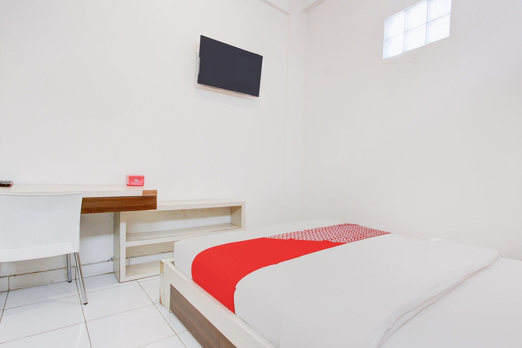 Ein Zimmer mit einem Bett, einem Schreibtisch, einem Stuhl, einem an der Wand befestigten Fernseher und einem Fenster.