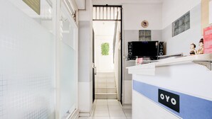 Ein Hotel-Empfangsbereich mit Fliesenboden, einer Rezeption mit der Aufschrift 'OYO', einer Treppe, die zu einem Außenbereich führt, und einem an der Wand befestigten Fernseher.
