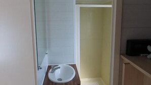 Un bany amb un lavabo blanc, un espai de banyera amb envidriat i un moble de tocador de fusta.