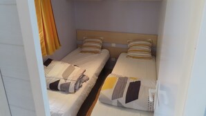 Habitació petita amb dos llits, un frontal de fusta i una cortina groga.