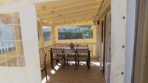 Un balcó cobert amb taula i cadires de fusta, vista cap a vegetació, i una porta amb finestre.