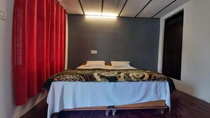 Una cama individual con una colcha estampada, un mantel blanco y una cortina roja.