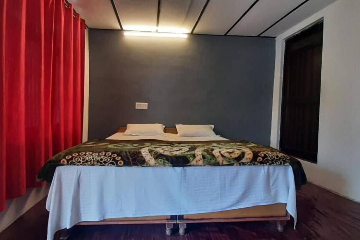 A single bed with a patterned bedspread, a white tablecloth, and a red curtain.