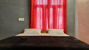 Een kamer met een bed, een stopcontact en een raam met rode gordijnen.