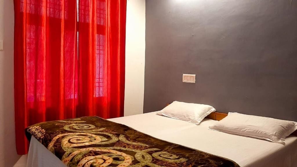 Un letto singolo con una coperta fantasia, un cuscino bianco e una tenda rossa.