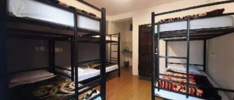 Une pièce avec des lits superposés, un plancher en bois et une porte donnant sur une autre pièce.