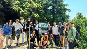 Un grupo de personas de pie sobre un sendero de tierra con un letrero que dice 'WELCOME TO TRIUND TREK'.