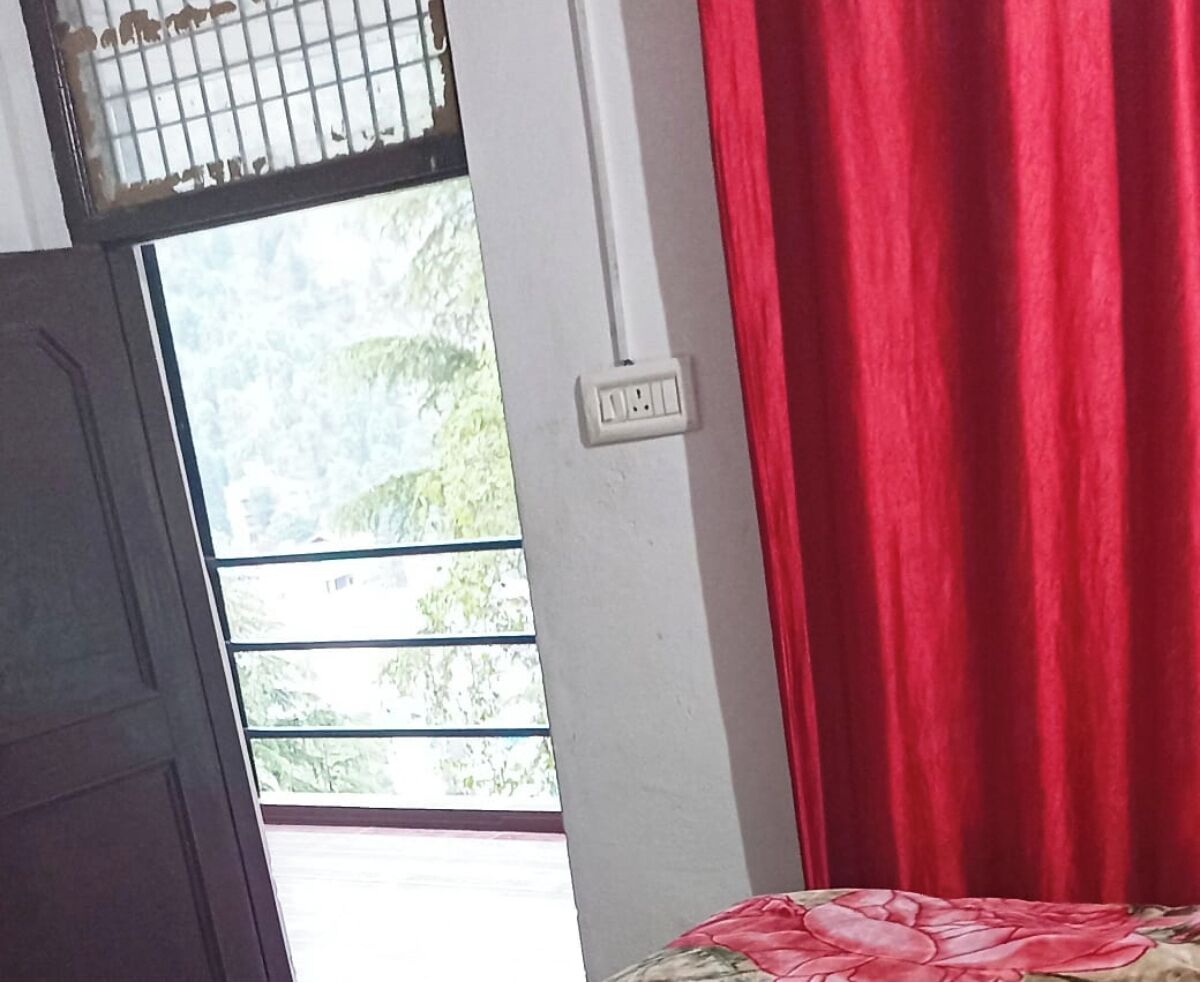 A room with a window, a power outlet, and a red curtain.