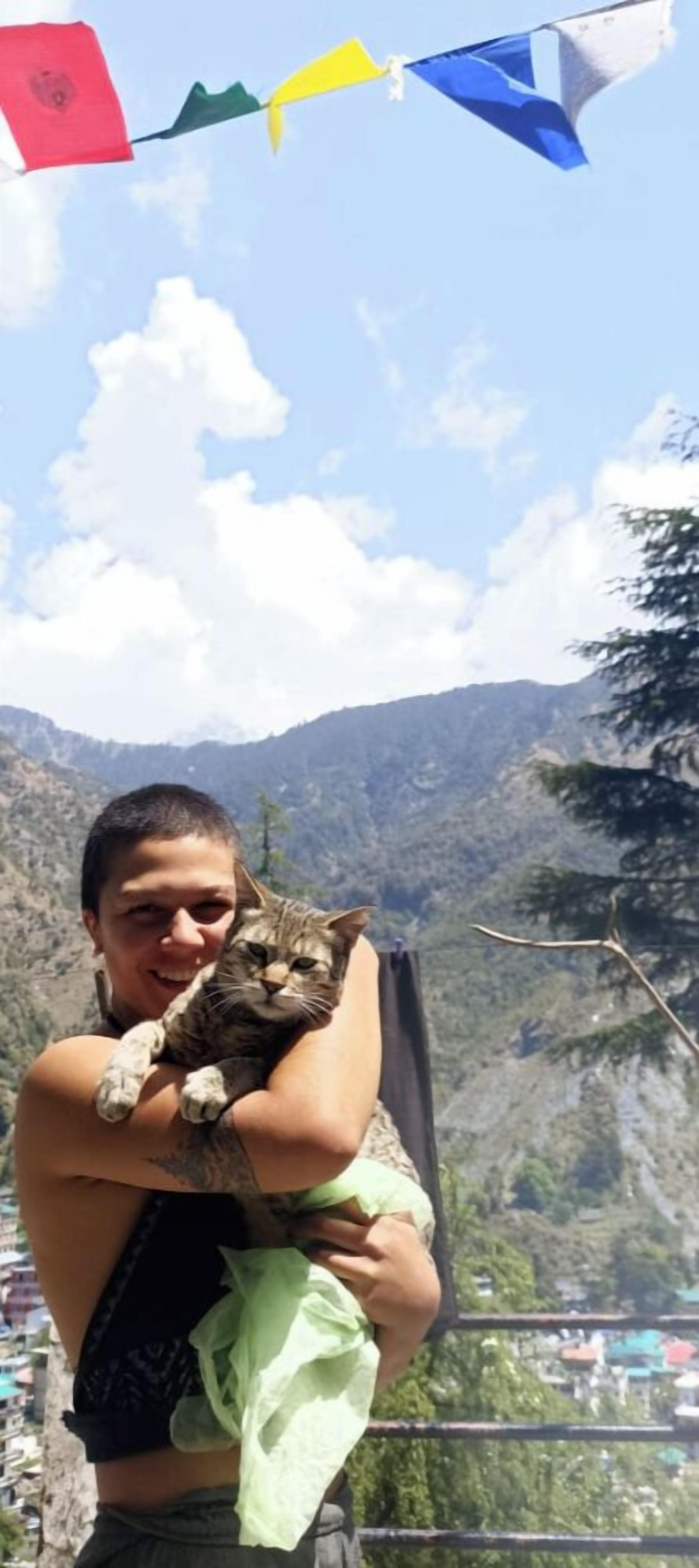 A person holding a cat with a mountainous landscape in the background.