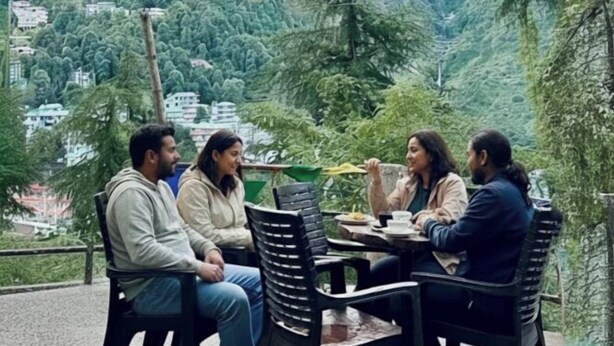 Un grupo de personas sentadas en una mesa al aire libre, con un paisaje montañoso de fondo.