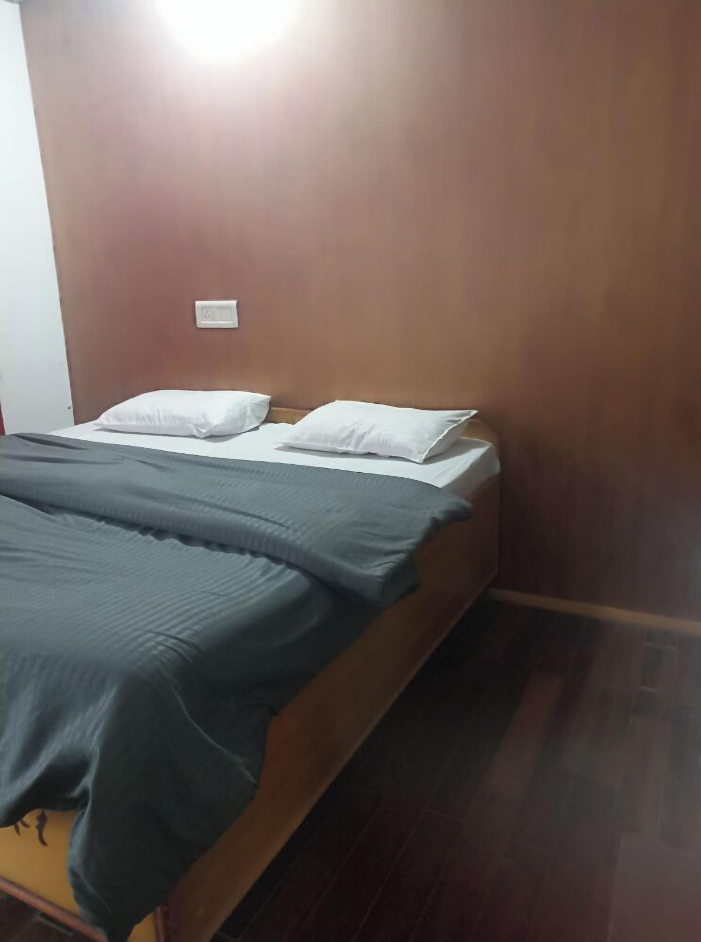 A single bed with a wooden frame, a grey bedspread, and two white pillows.
