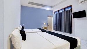 Ett hotellrum med två sängar, en platt-TV och ett fönster med gardiner.