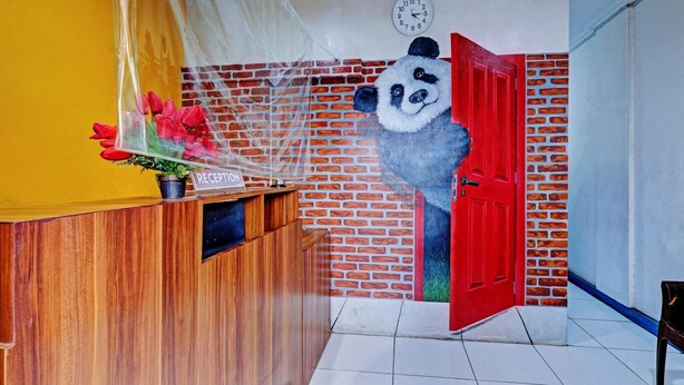 Un comptoir d’accueil orné d’une fresque représentant un panda, une horloge et une porte rouge.