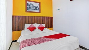 Une chambre d’hôtel avec un lit, une tête de lit en bois, un tableau encadré au mur et une couvre-lit à motifs rouges et blancs.