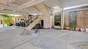 Ein überdachter Parkbereich mit einer Treppe zu einem Hauseingang, einige abgestellte Motorräder und Topfpflanzen.