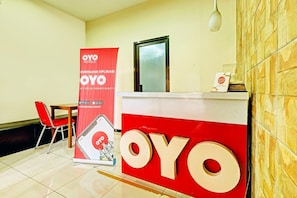 A hotel reception area with a red and white sign, a wooden chair, and a tiled floor.