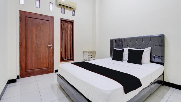 Een slaapkamer met een bed, een houten deur, een raam met gordijnen en een airconditioner aan de muur.