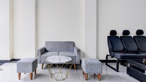 Een moderne kamer met een grijze bank, bijpassende voetenbankjes, een klein rond tafel met een marmeren blad, en een zwart zithoek met meerdere stoelen.