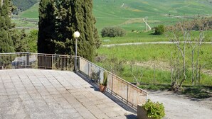 Eine gepflasterte Terrasse mit Geländer, mit Blick auf eine grüne Landschaft mit Bäumen und weit entfernten Hügeln.