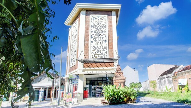 Un edificio con una torre central decorada con intrincados diseños blancos, rodeado de vegetación y un cielo azul despejado.
