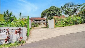 A gated entrance to a building with a concrete pathway leading to a door, surrounded by greenery and a clear sky.