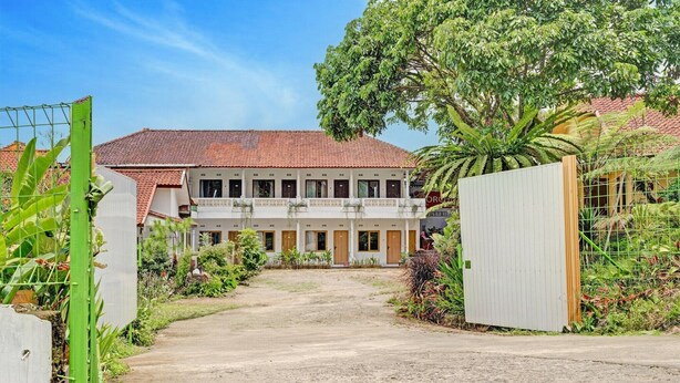 A building with a red-tiled roof, a central entrance, and a gated driveway.