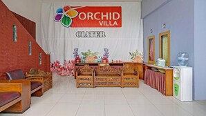 A room with a reception desk, wooden benches, a water dispenser, and a banner reading 'ORCHID VILLA CIATER'.