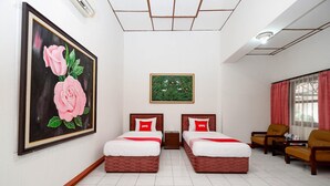 Een hotelkamer met twee bedden, een rozenstillife, een foto in een groene lijst en een raam met gordijnen.